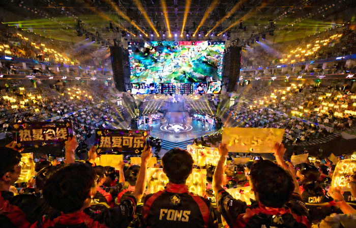 英雄联盟职业联赛线下赛场观众席全景，舞台大屏正在播放比赛实况画面